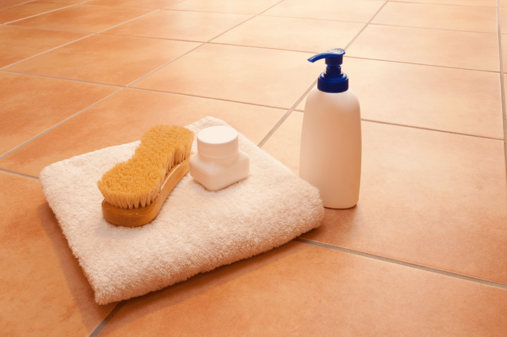 Un asciugamano, una spazzola e un prodotto poggiati sul pavimento in cotto