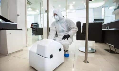 macchina per sanificazione ambiente in un ufficio con addetto alla sanificazione in tuta bianca e mascherina